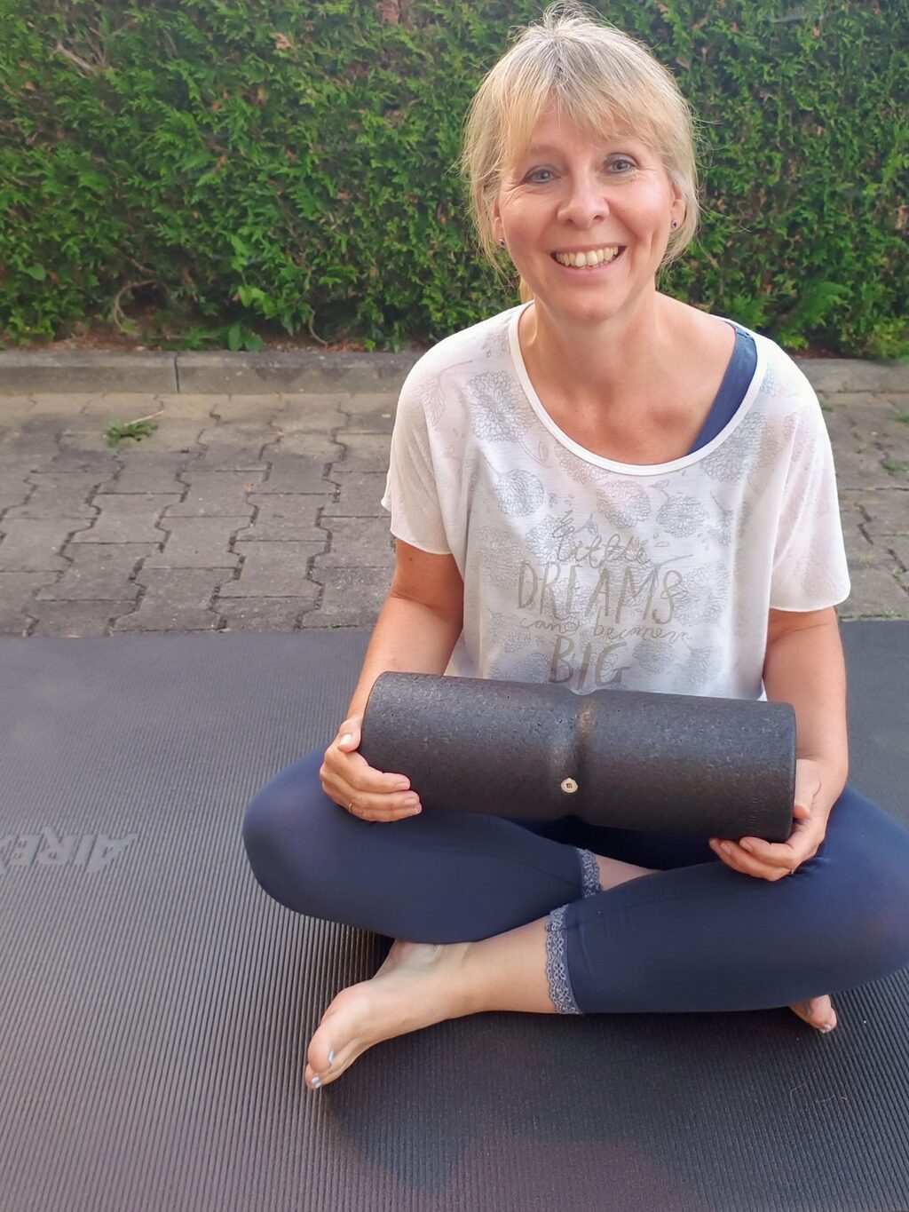 Melanie sitzt entspannt im Schneidersitz auf der Yogamatte und hält eine Faszienrolle.